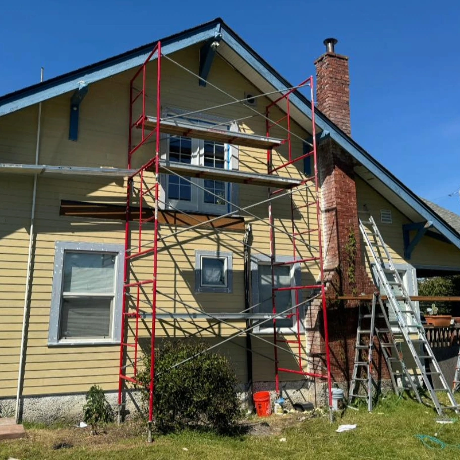 A home with scaffolding set up next to it where workers are removing and replacing siding.